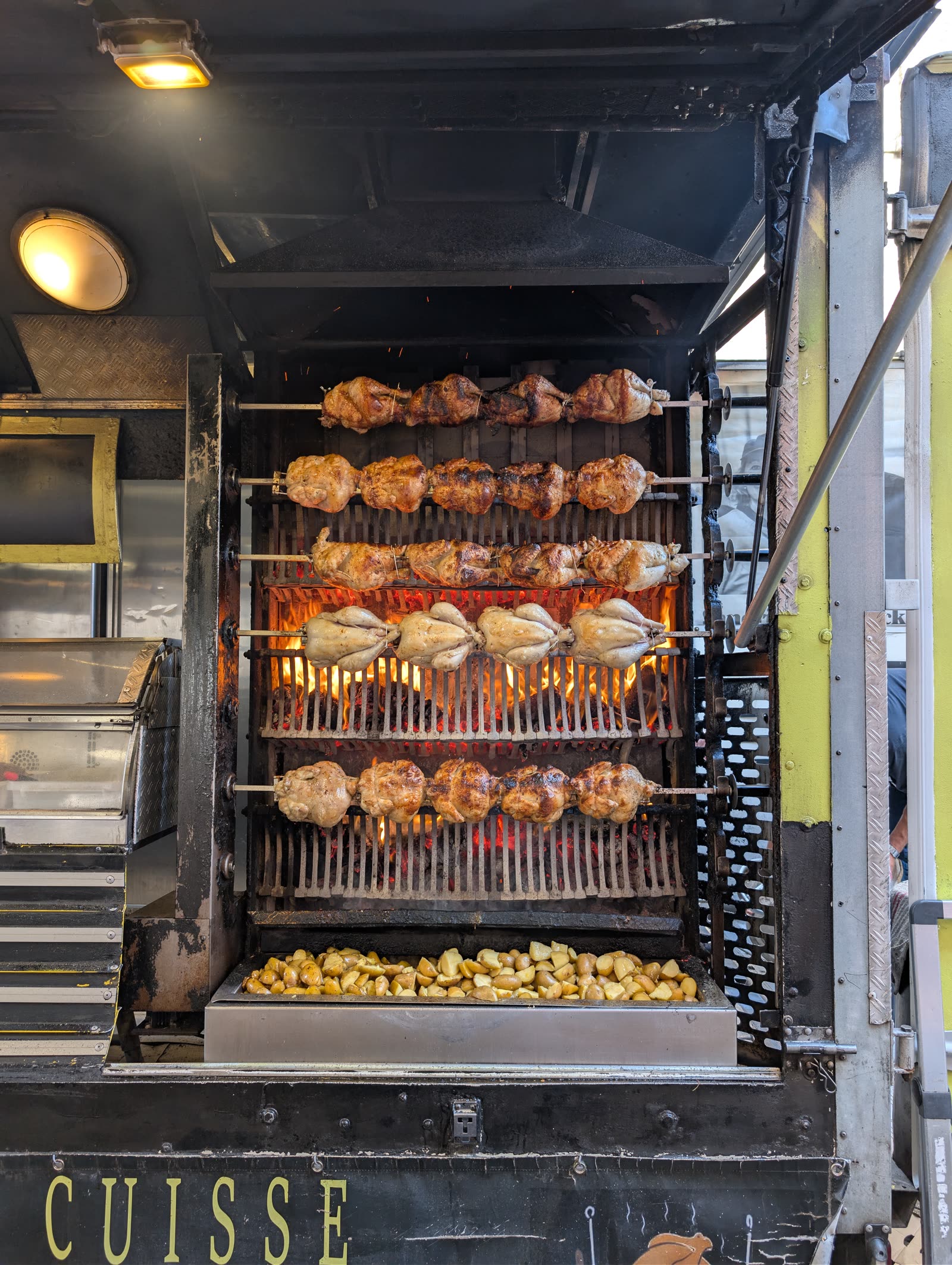 Whole chickens turning on rotisserie spits inside a lit supermarket display cabinet.