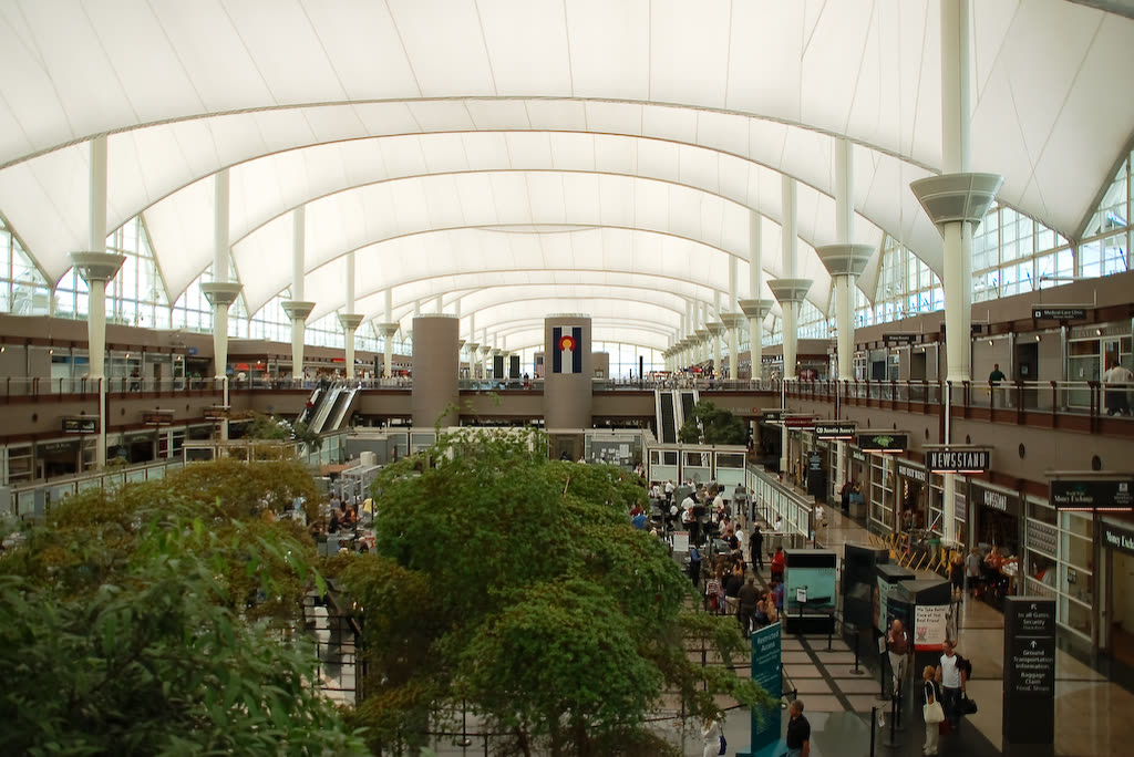 The exterior of the Denver International Airport terminal, showing its white peaked tent roof against the sky.